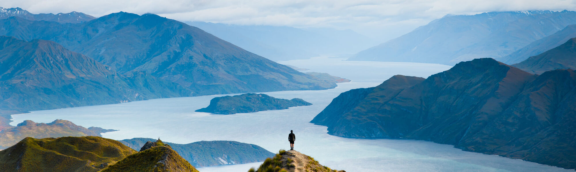 Person standing alone on a ridge overlooking Lake Wanaka and mountains